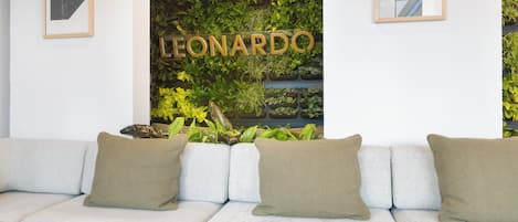 A modern interior with a light grey sofa, a wall-mounted plant display, and a framed sign that reads "LEONARDO".