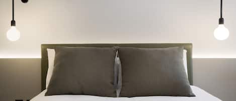 Cama bem arrumada com cabeceira verde e duas almofadas, iluminada por duas lâmpadas pendentes.