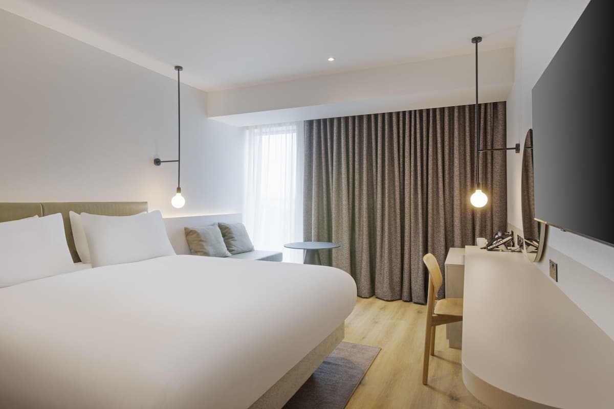 A modern hotel room with a large bed, a desk, and a TV.