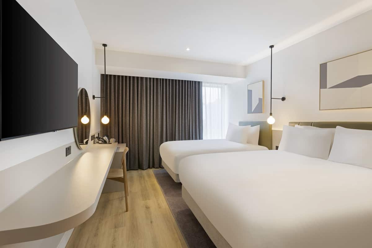 A hotel room with a large bed, a desk with a flat-screen TV, a chair, and a large window with curtains.