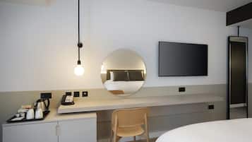 Una habitación de hotel moderna con una cama, un escritorio con una silla, un espejo redondo, un televisor de pantalla plana y una estación de café.