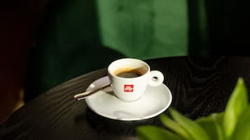 A cup of coffee on a saucer with a spoon, a cup of latte with a heart design, and a green plant on a table.
