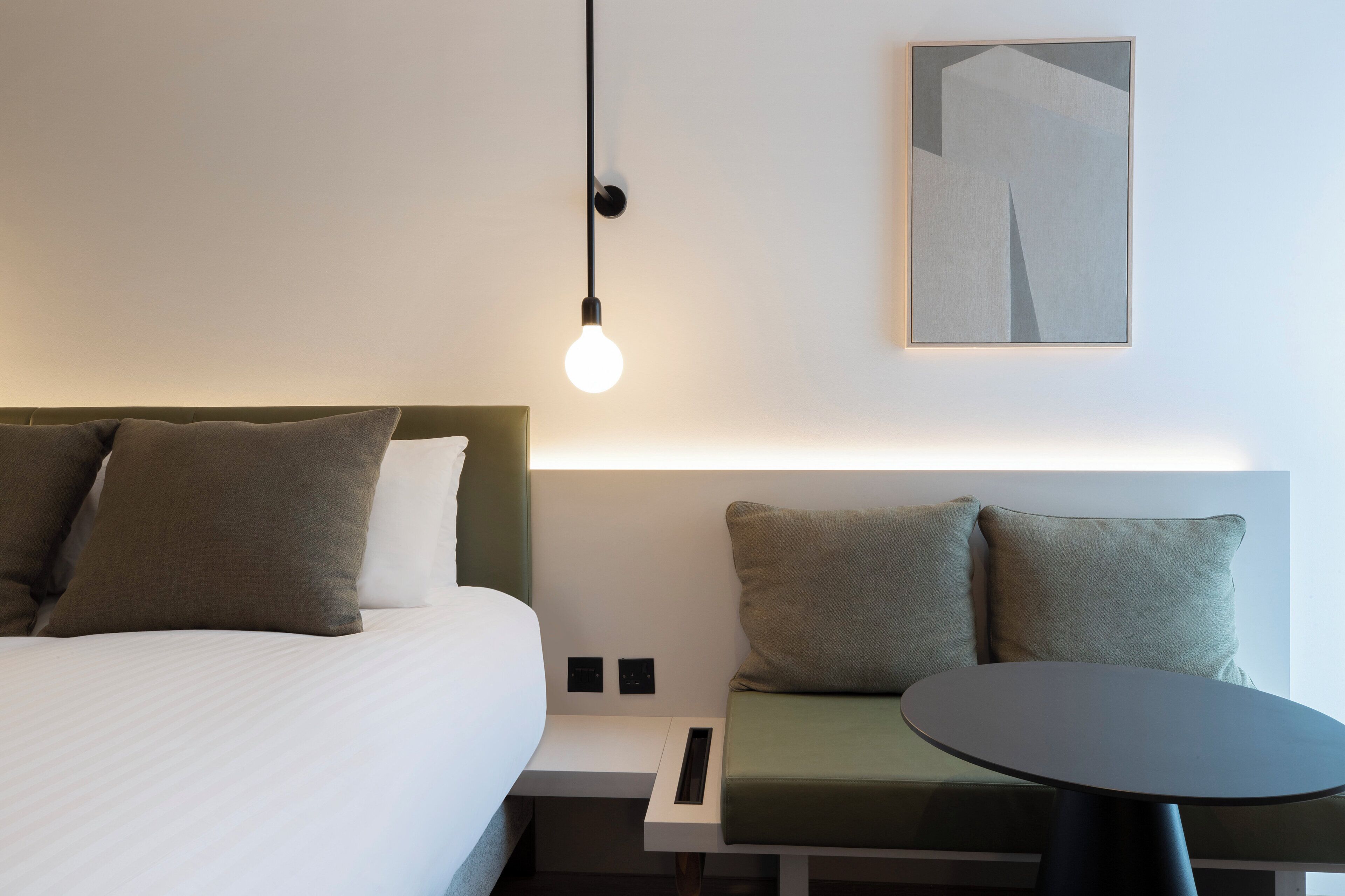 A hotel room with a bed, bedside table, and a wall-mounted light fixture.