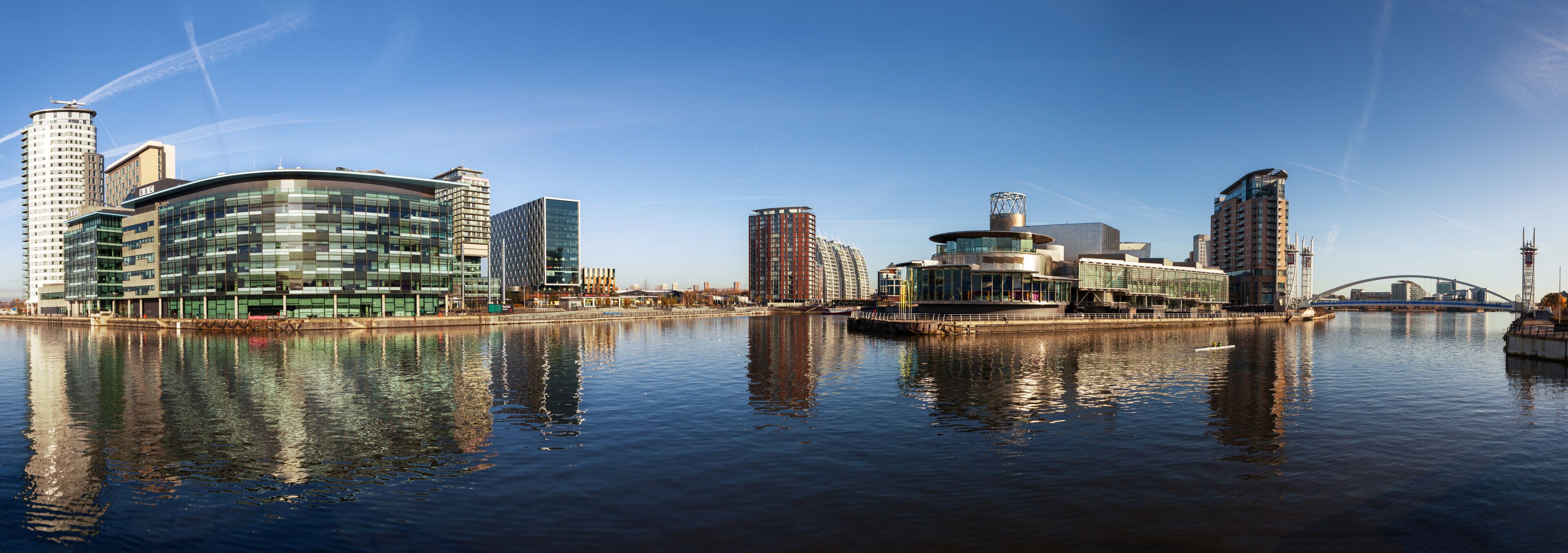 A waterfront cityscape with modern buildings, a river, and a bridge.
