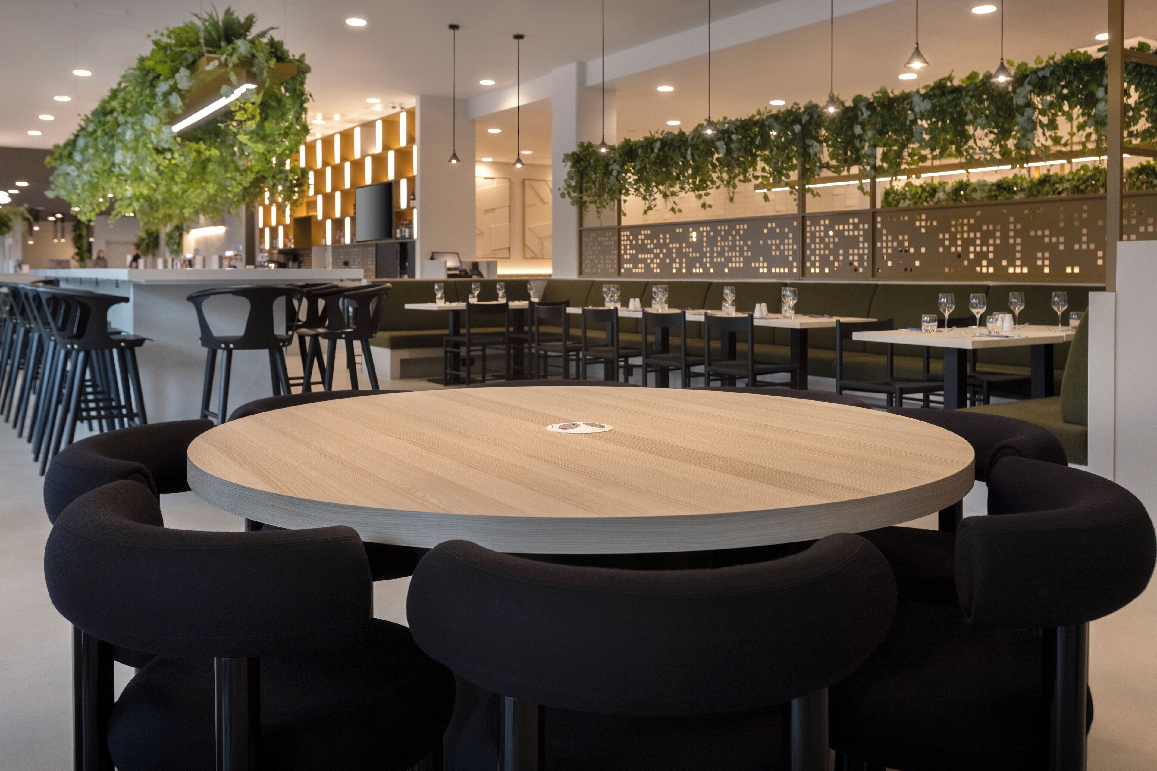 A modern restaurant with round tables, black chairs, and hanging plants.