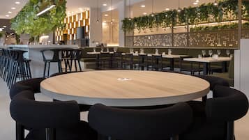 A modern restaurant with round tables, black chairs, and hanging plants.