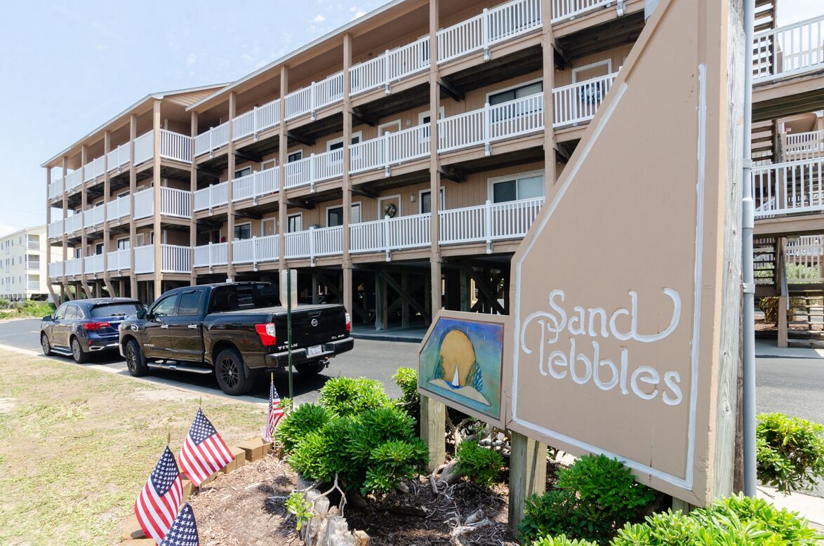 Un hôtel à plusieurs étages doté de balcons, une enseigne indiquant « Sand Pebbles », et des drapeaux américains au premier plan.