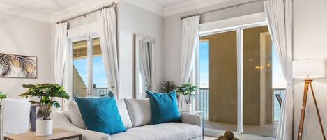 A modern living room with a sofa, a coffee table, and a view of the ocean through large windows.