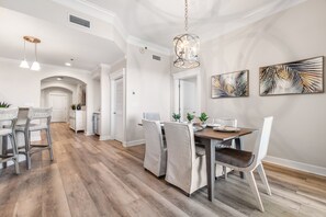 Un comedor moderno con suelo de madera, sillas blancas, una mesa de madera e iluminación colgante.