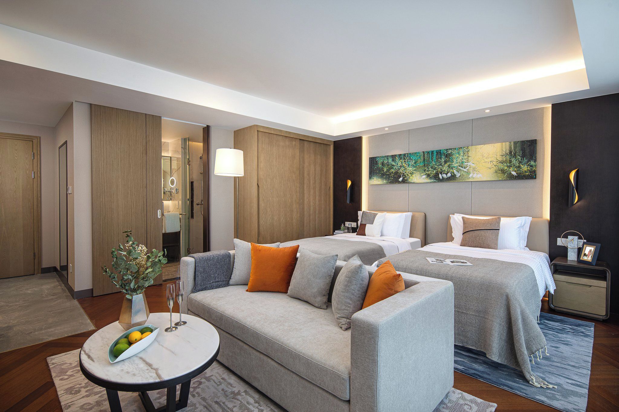 A hotel room with a sofa, two beds, a dining table, and a painting on the wall.