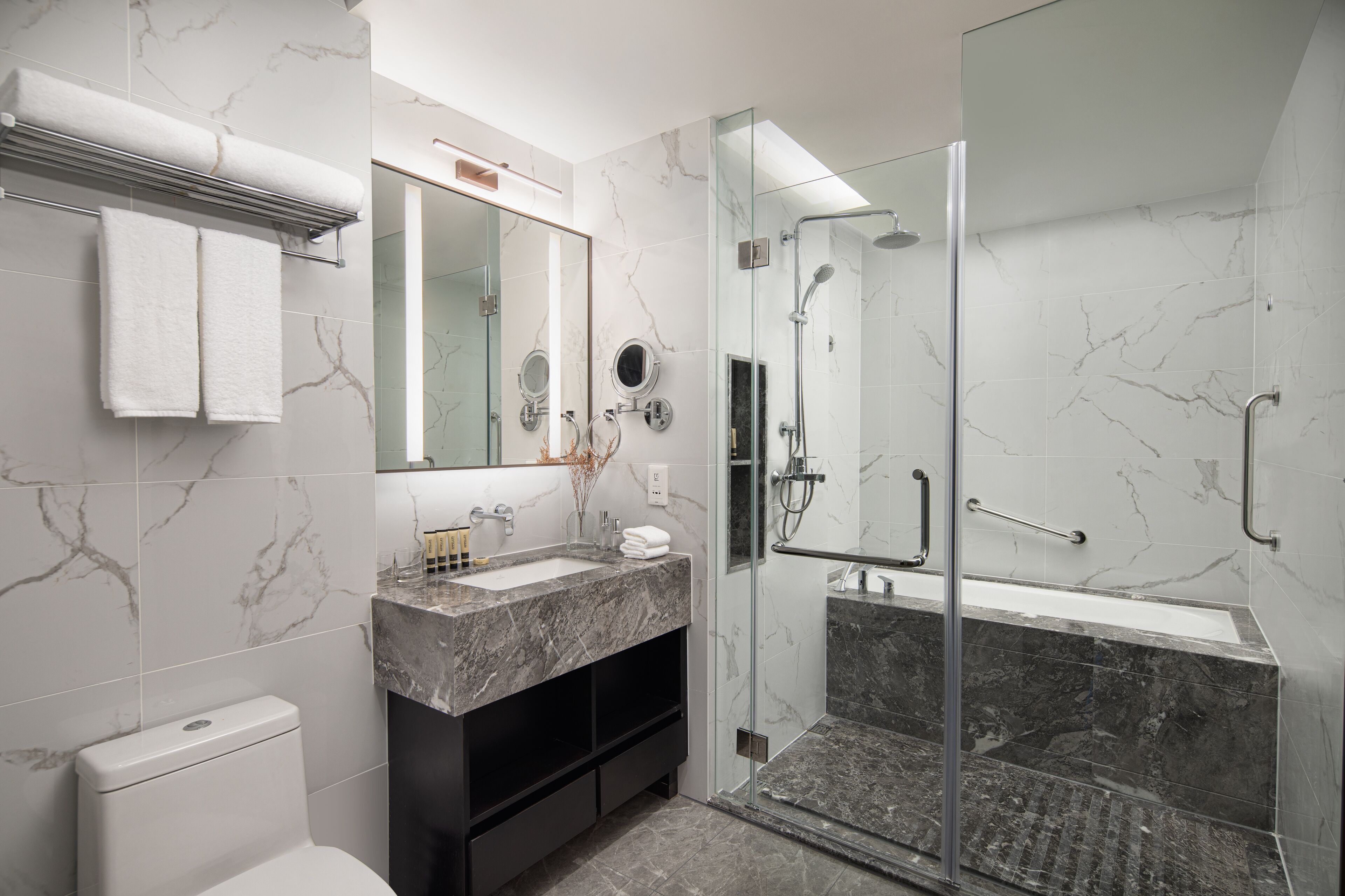 A modern bathroom with a glass-enclosed shower, a marble sink, and a large mirror.