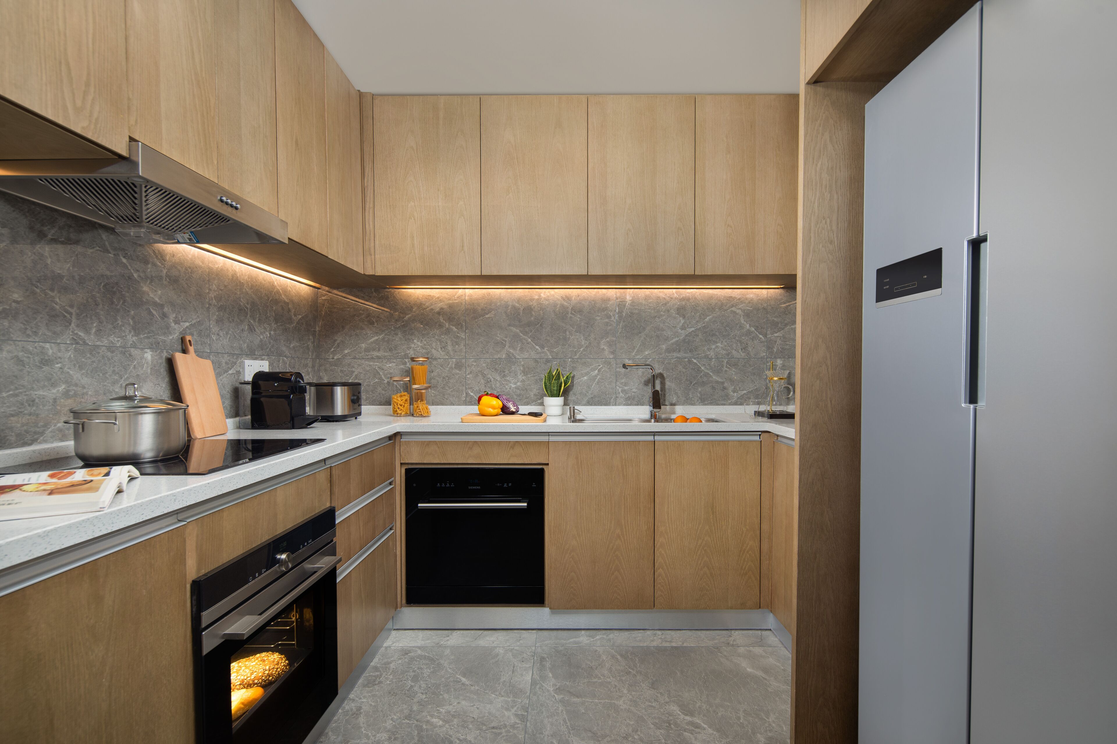 Una cocina moderna con armarios de madera, horno empotrado, lavavajillas y refrigerador de acero inoxidable.
