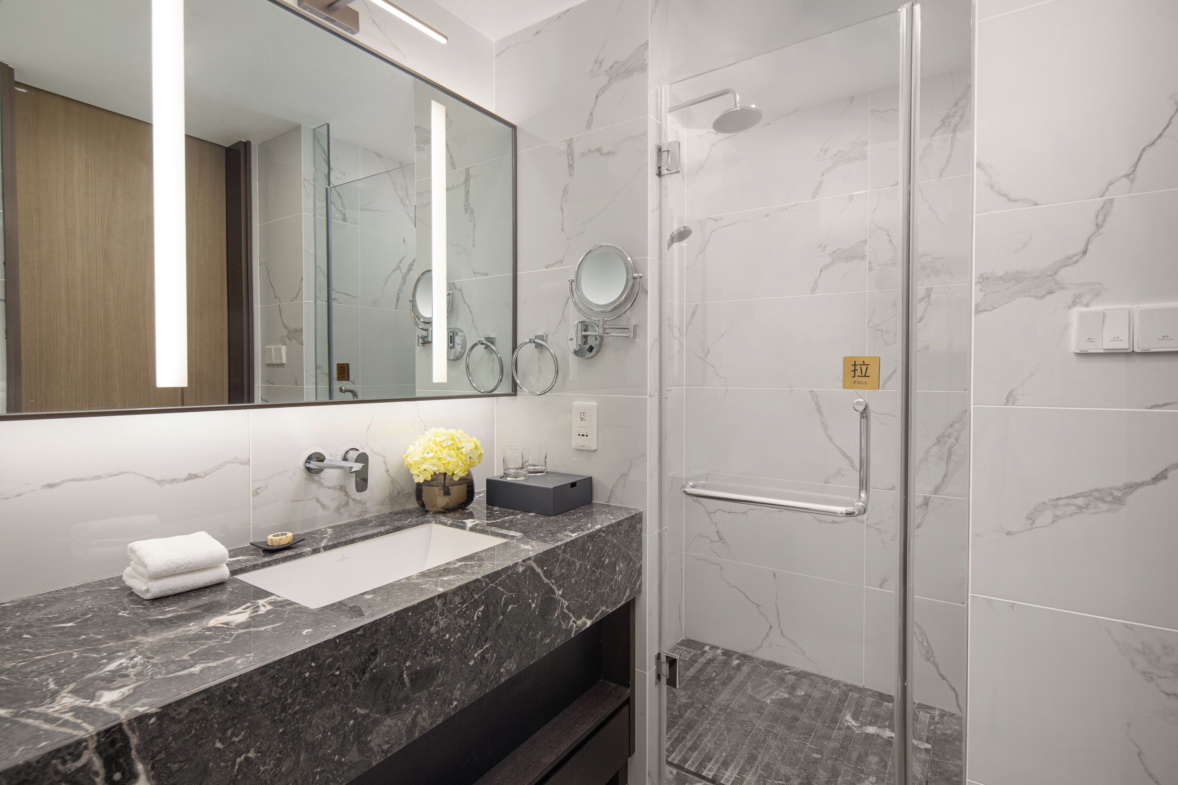 Un baño moderno con lavamanos de mármol, un espejo grande y una cabina de ducha con paredes de vidrio.