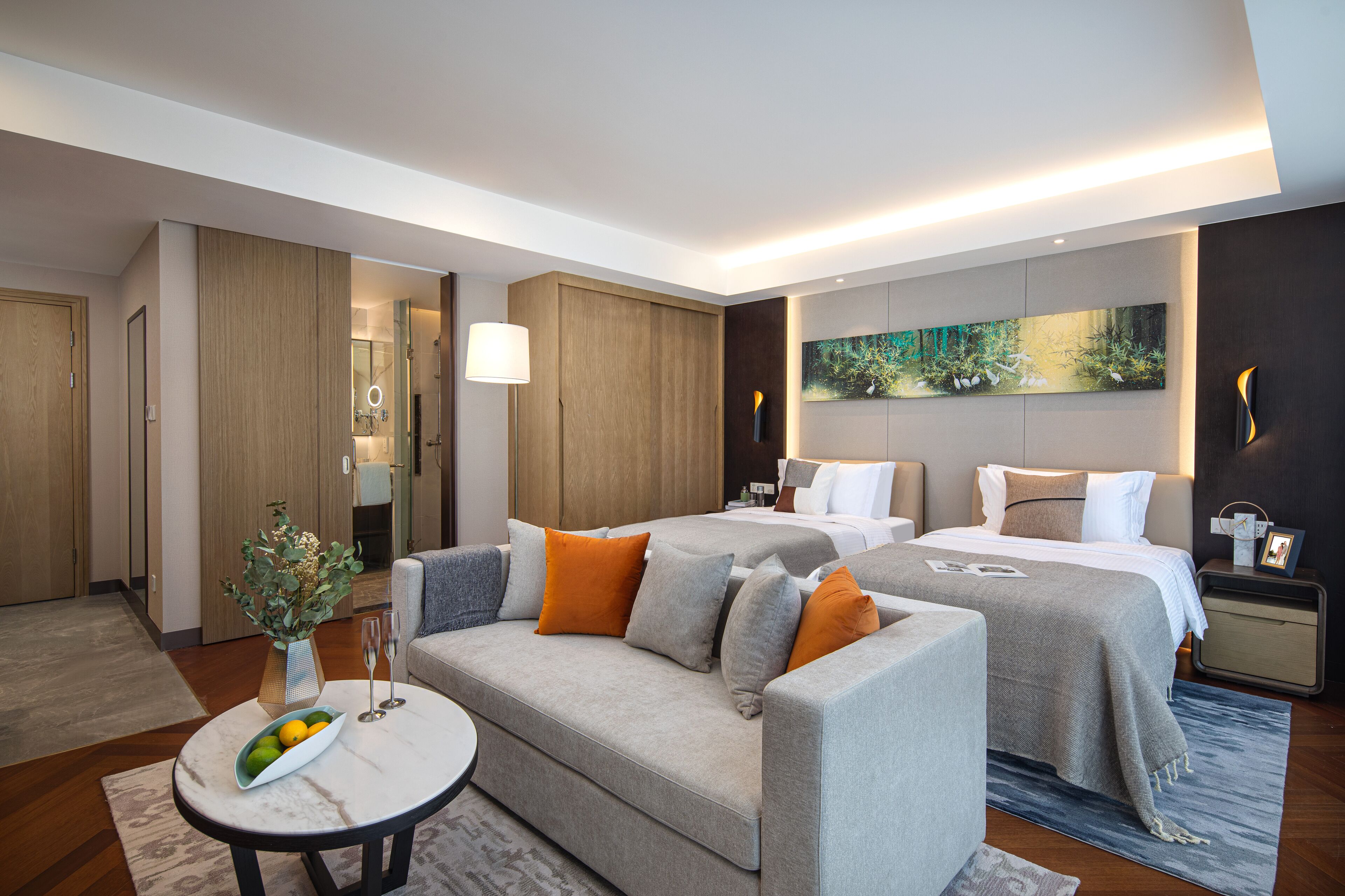 A modern hotel room with a sofa, two beds, a small table, and a painting on the wall.