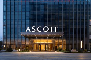 Um edifício moderno com o nome "ASCOTT" em destaque sobre a entrada.