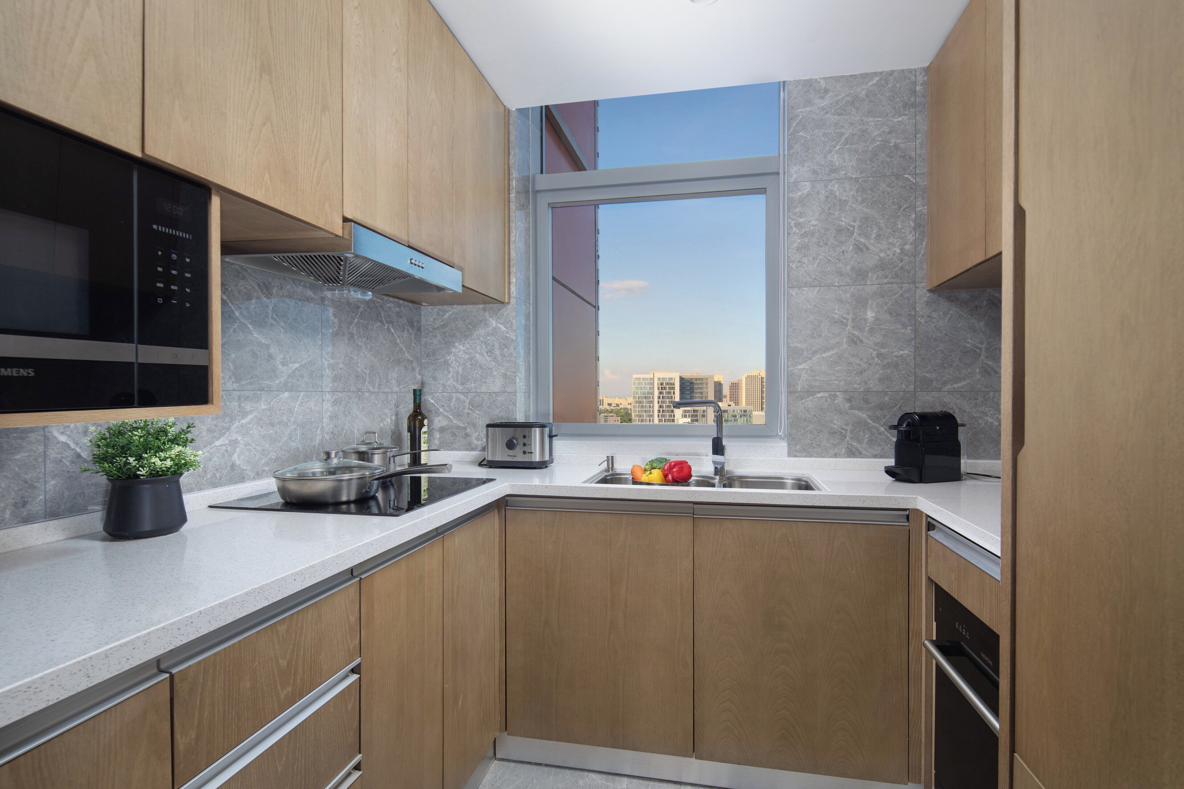 A modern kitchen with wooden cabinets, a built-in microwave, and a window with a city view.