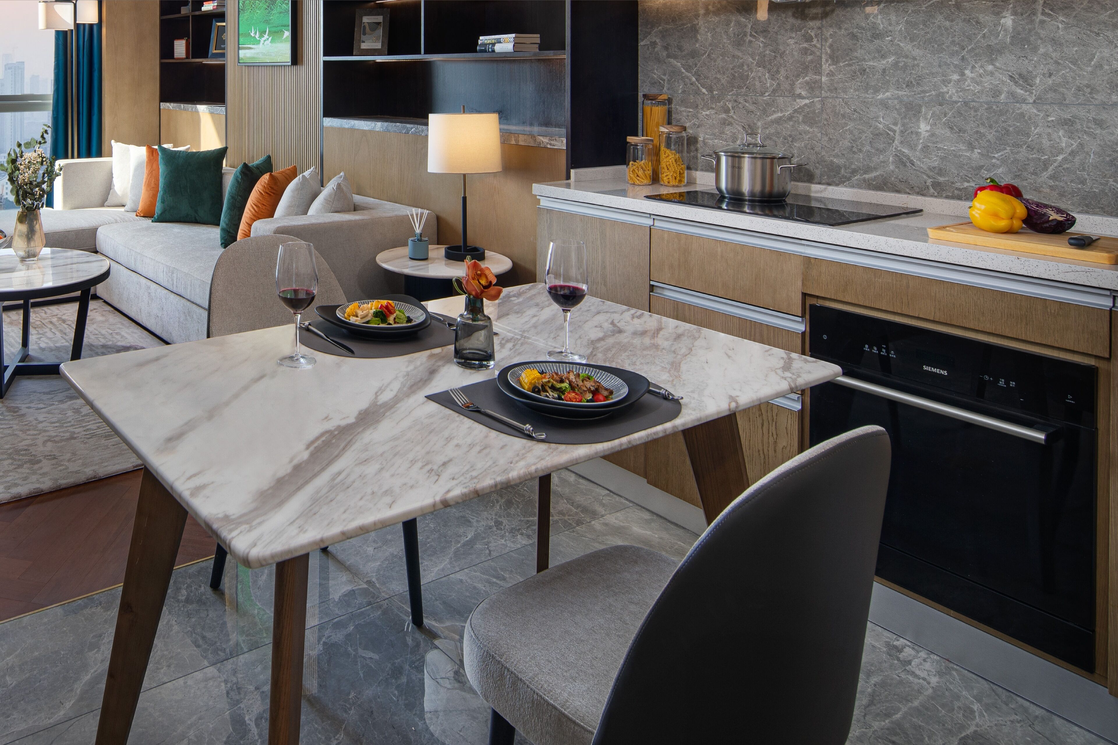 A modern kitchen with a dining area, marble countertops, and a built-in oven.