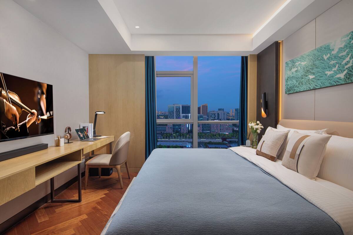 Une chambre d’hôtel moderne dotée d’un grand lit, d’un bureau, d’une télévision et offrant une vue sur la ville.