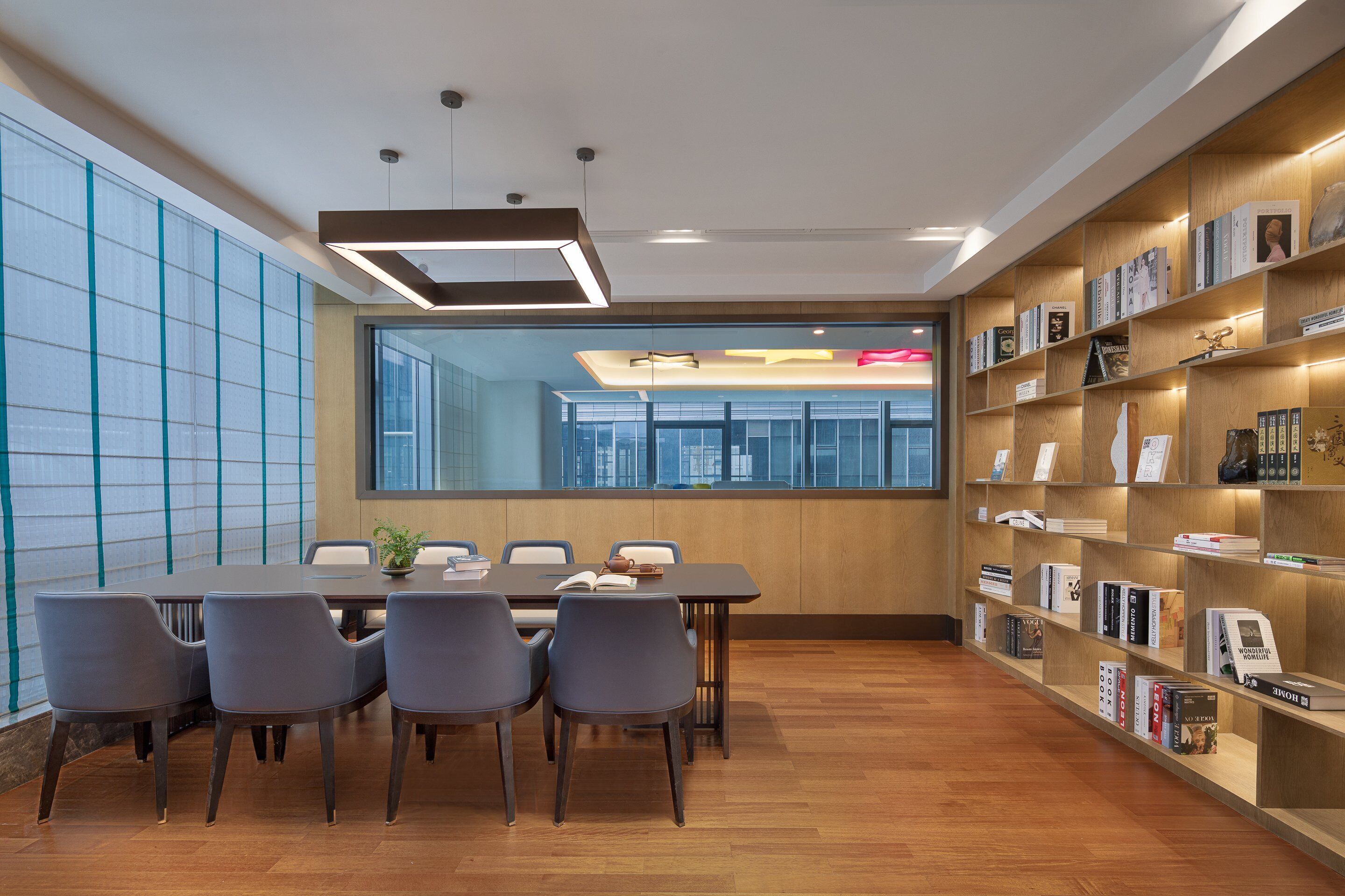 A modern conference room with a large table, chairs, and a bookshelf with books.
