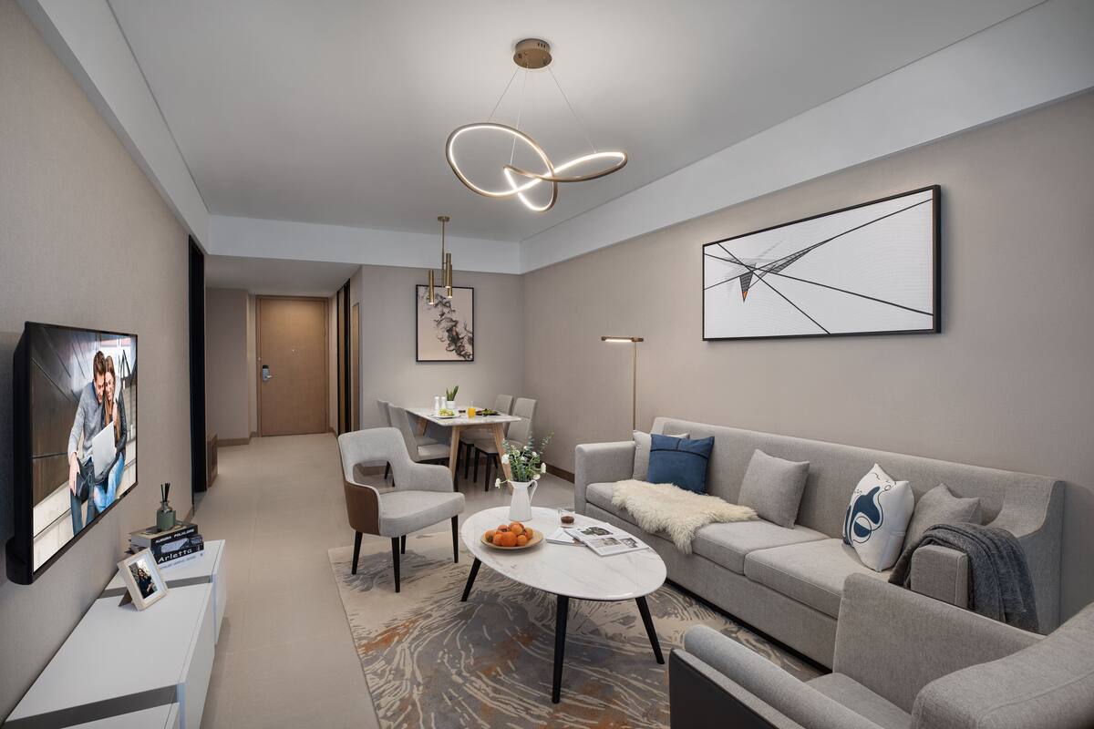 A modern living room with a sofa, coffee table, and TV. There is a dining area with chairs and a table.