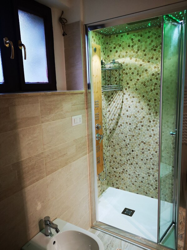 Une douche fermée par des parois de verre décorées d’un motif floral, un lavabo blanc et une porte en bois avec une poignée.