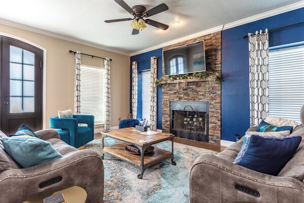 A living room with a fireplace, a ceiling fan, and a blue accent wall.