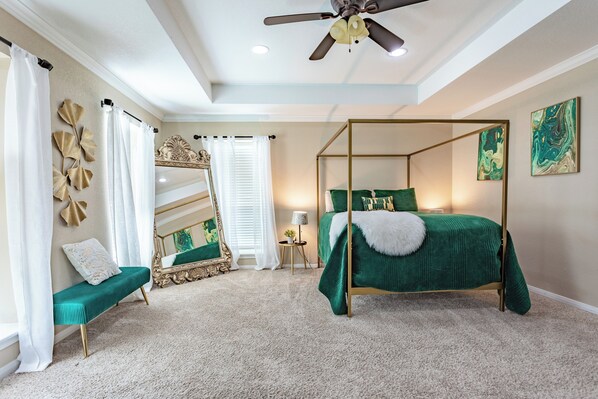 A four-poster bed with a green bedspread, a bench with a white cushion, and a ceiling fan.