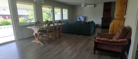 A spacious living room with a wooden dining table, chairs, a sofa, and a TV.