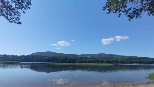 A calm lake with a sandy beach, surrounded by forested hills under a clear sky. - Lagomhuset - A Peaceful Holiday In Swedish Lapland (Vidsel)
