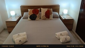 A neatly made bed with two pillows, two bedside tables with lamps, and a framed artwork above the bed. - Apartment Huerta del Obispo (Cádiz)