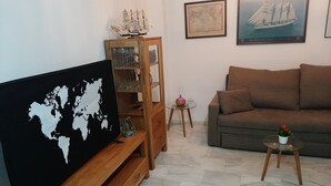 A living room with a wooden TV stand, a glass coffee table, a brown sofa, and a small table with a plant. - Apartment Huerta del Obispo (Cádiz)