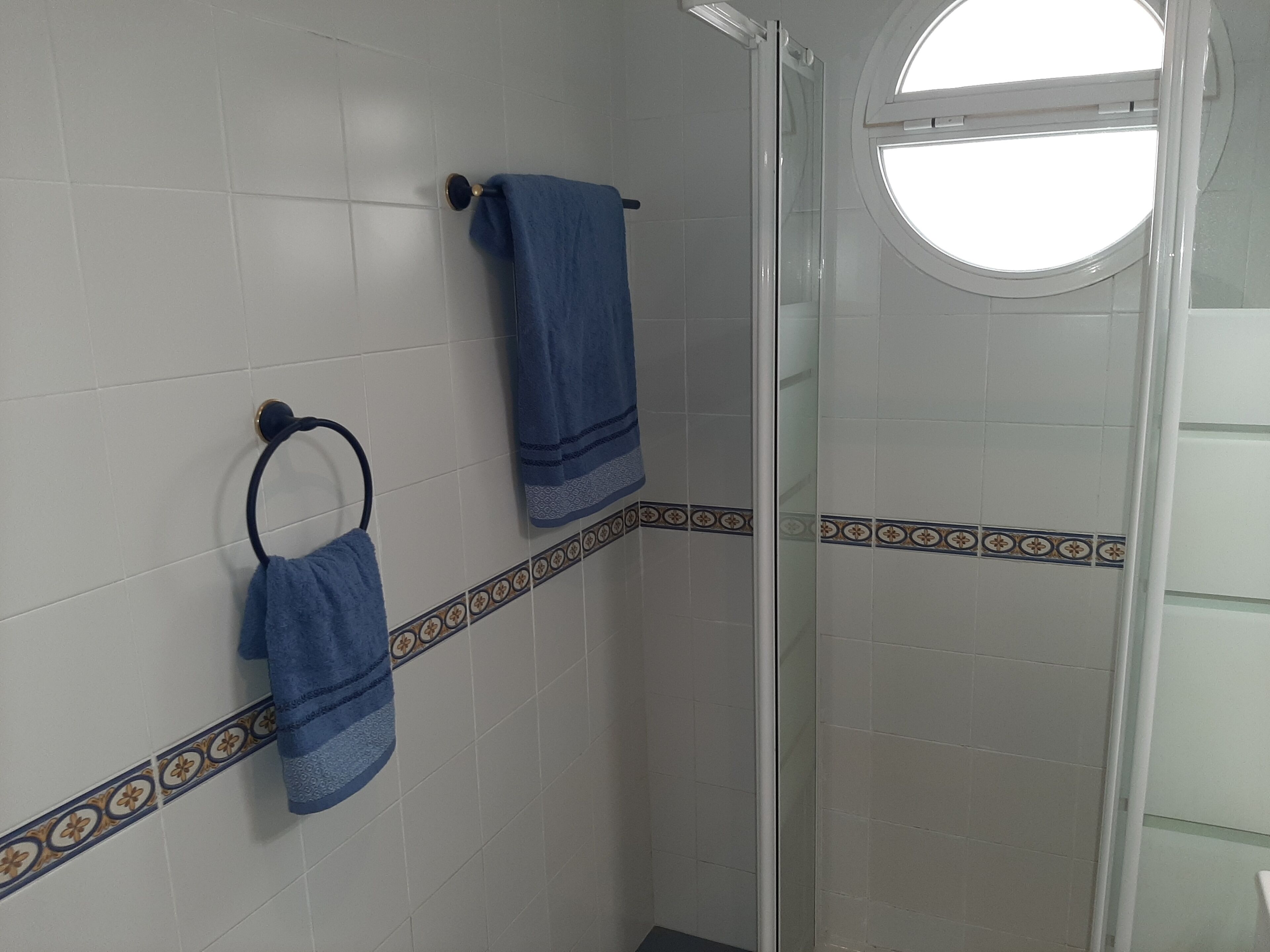 A bathroom with white tiles, a glass shower enclosure, and a window.