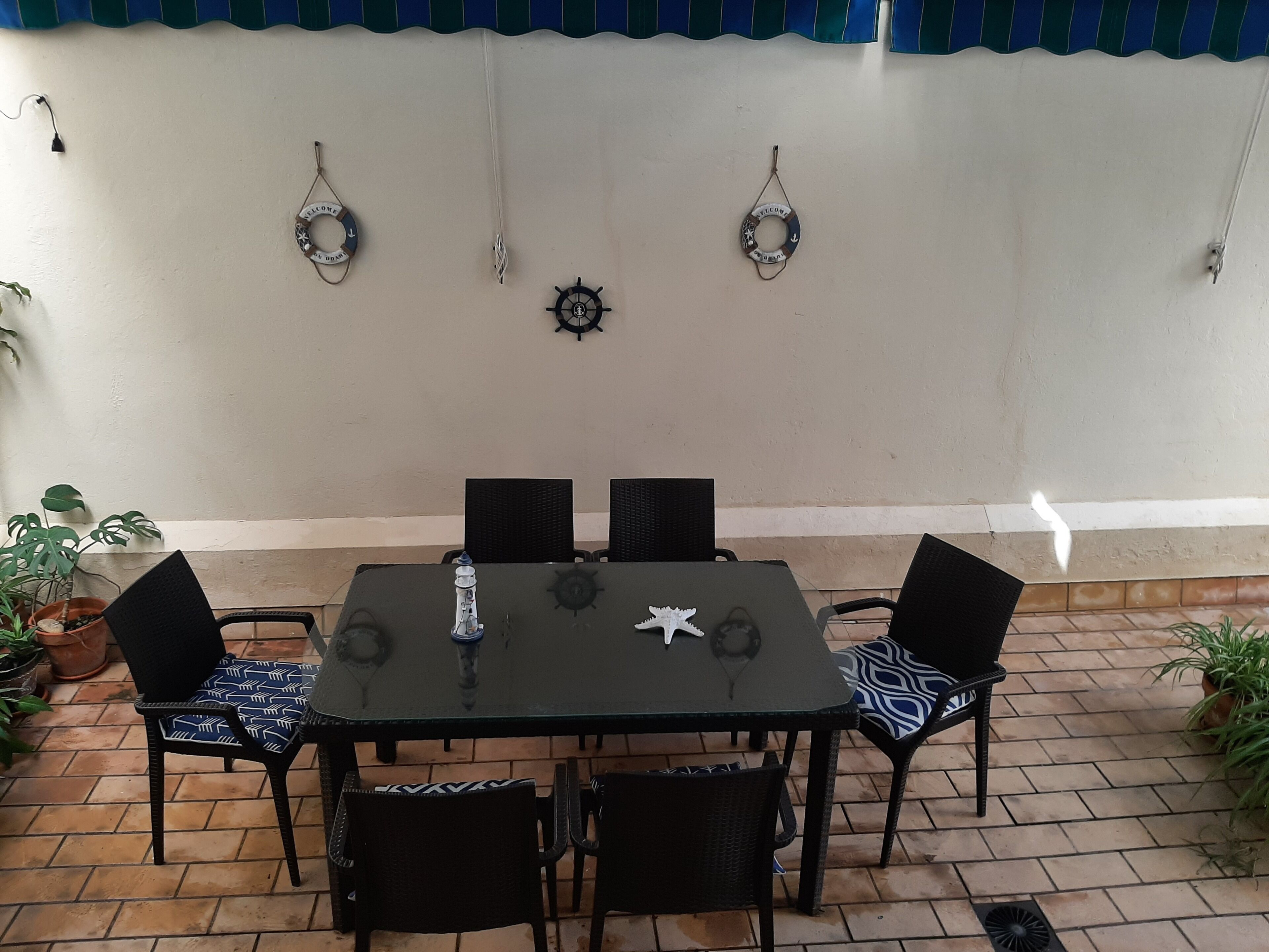 A patio with a table and chairs, potted plants, and wall decorations including a life ring and a ship's wheel.