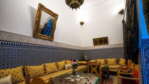 A room with a patterned blue and white tiled wall, a yellow patterned sofa, a round table with a vase, and a large mirror. - Room in B&B - Riad Authentic Palace & Spa -jawhara (Fes)