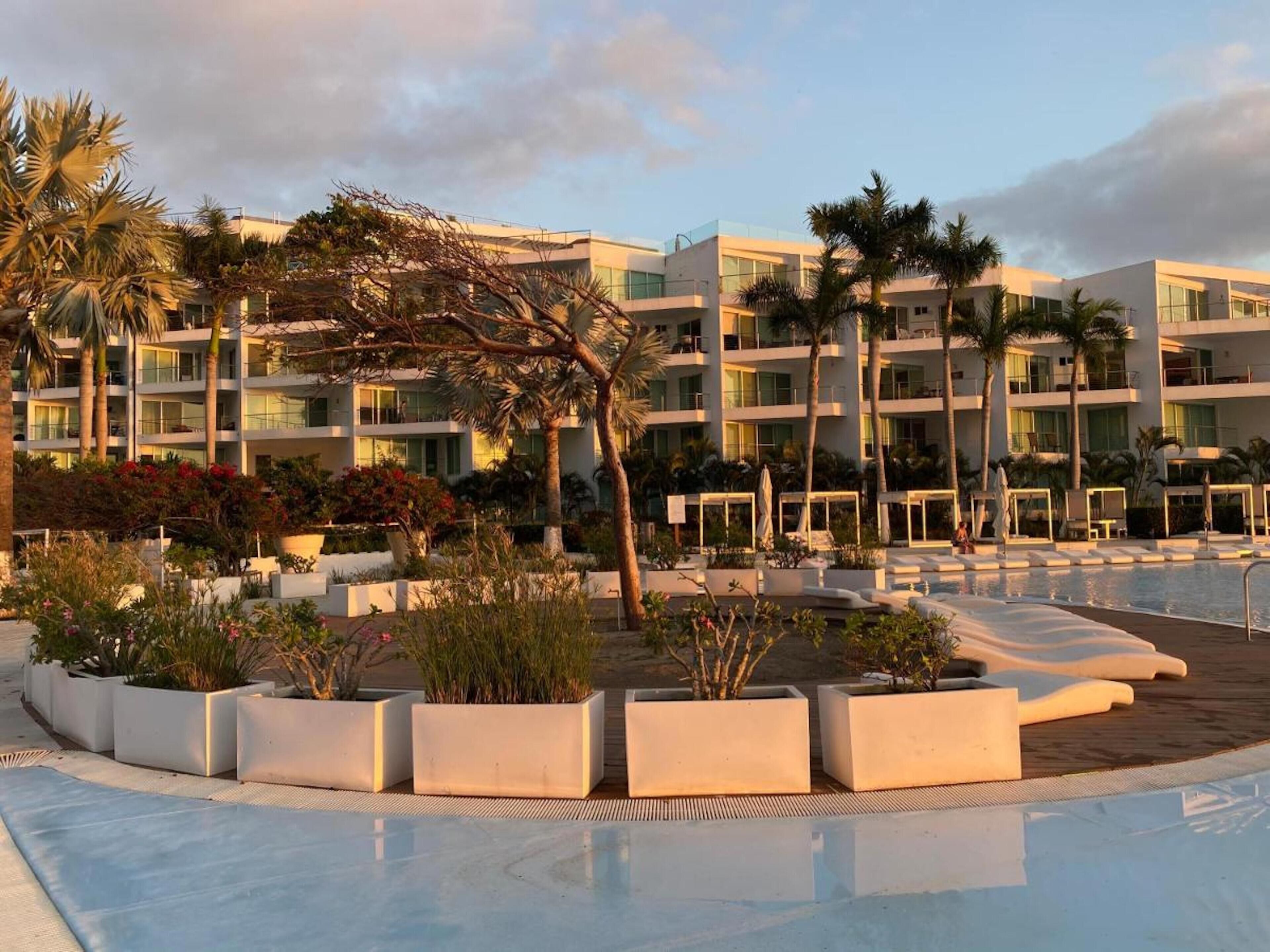 Un complexe hôtelier doté d’une piscine, de palmiers et d’un immeuble à plusieurs étages avec des balcons.
