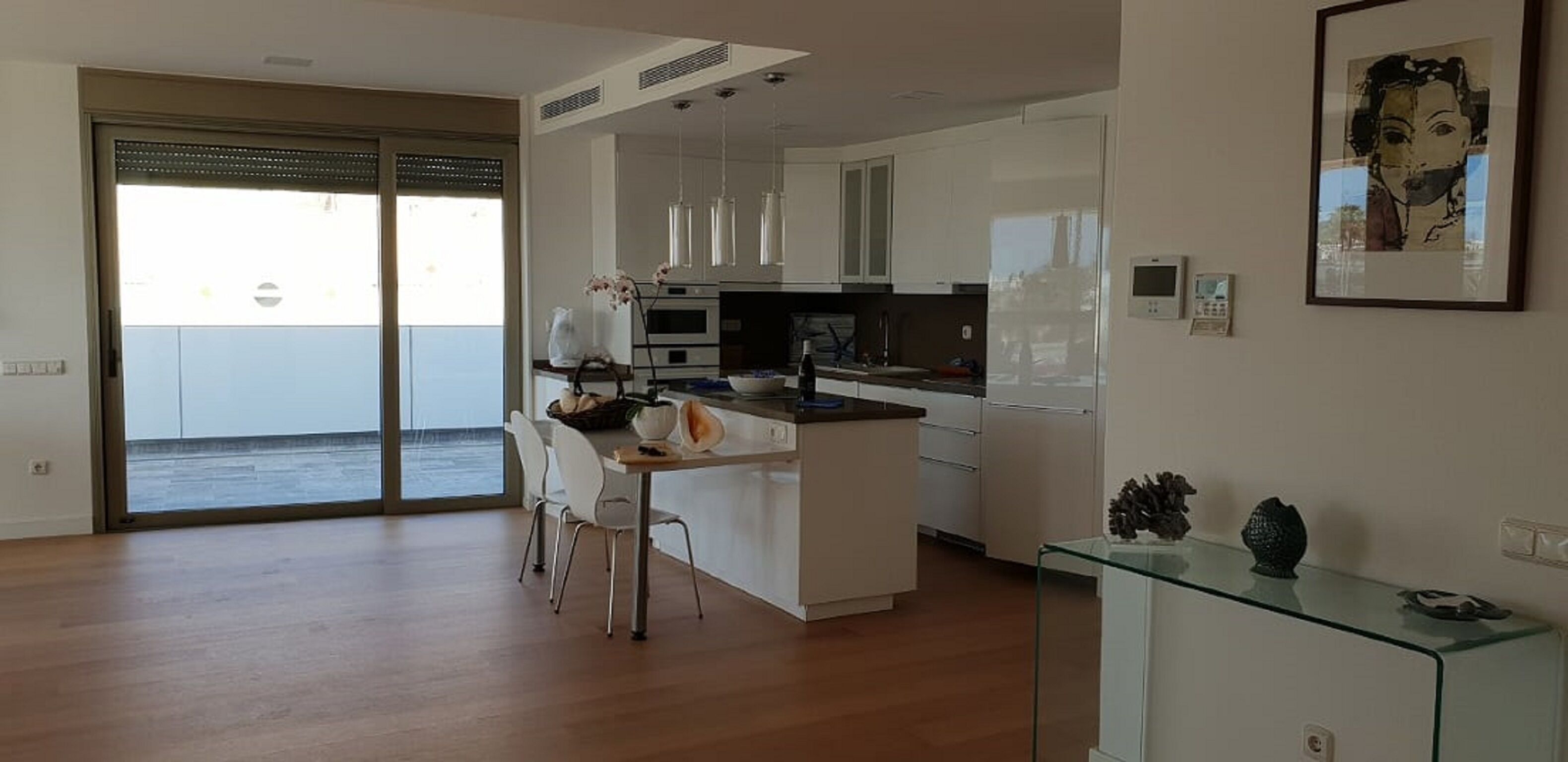 A modern kitchen with white cabinets, a central island, and a dining area with chairs.