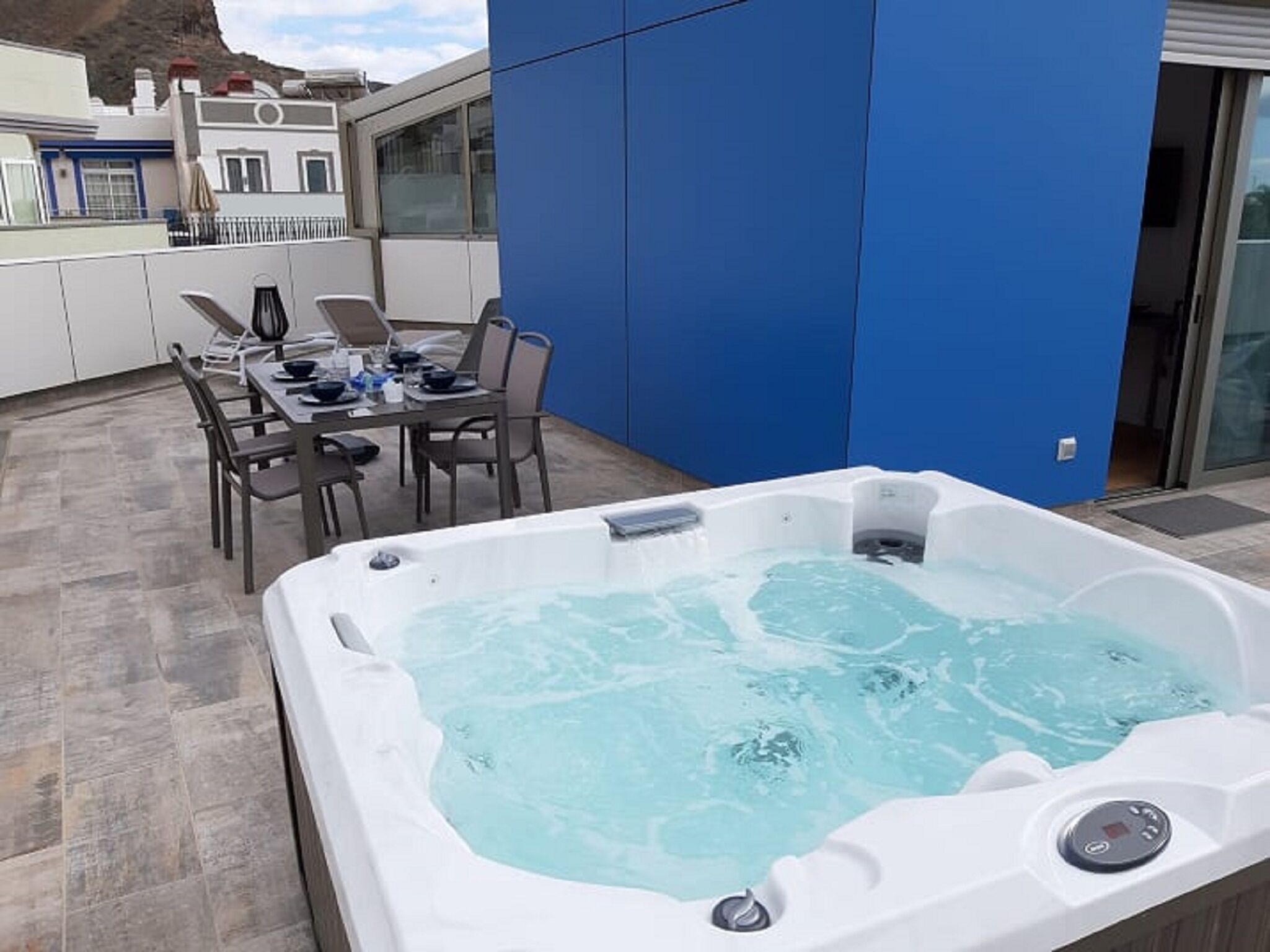 A modern outdoor area with a hot tub, dining table, and chairs.