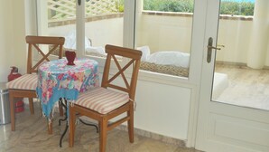 A room with a table and chairs, a bed, and a view of a mountainous landscape through large windows. - House Lemoni, Apartment B - Pelekas, Corfu (Corfu)