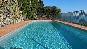 Ein rechteckiger Pool mit klarem, blauem Wasser, umgeben von einer Steinmauer und einem Metallzaun.