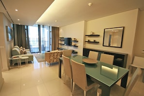 A modern living room with a glass dining table, beige chairs, a sofa, and a TV. - One Bedroom Apartment - Fully Equipped Waterfront Based, V&a Marina Residential (Cape Town)