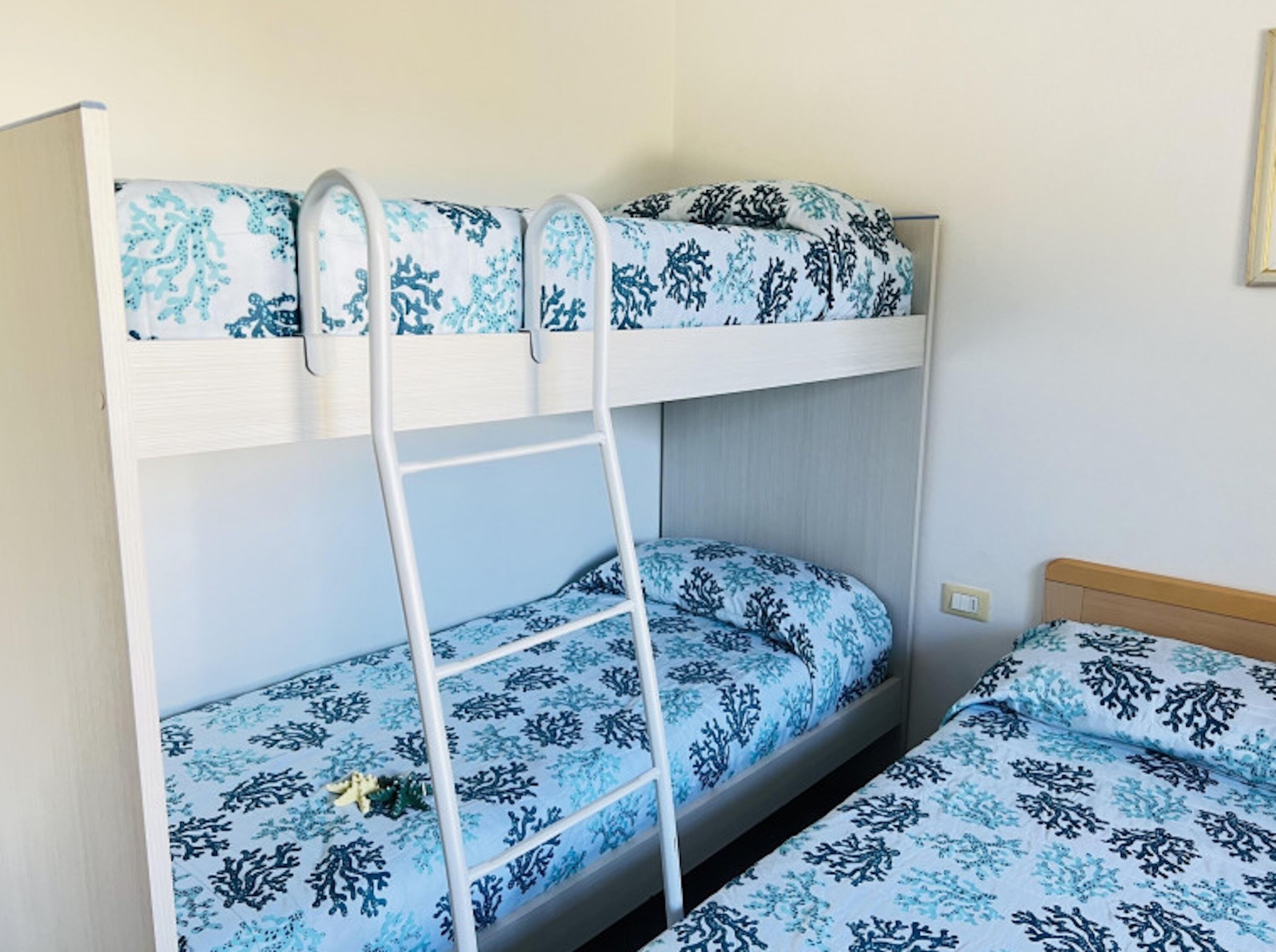 Ein Etagenbett mit einer Leiter, blauer Bettwäsche mit Muster und einem Holz-Kopfteil.