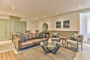 Un salon moderne avec un canapé en cuir, une table basse en verre, un tapis à motifs et une cheminée.
