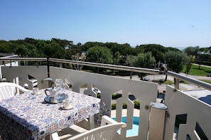 A balcony with a table set for two, overlooking a pool and a park. - Studio With Shared Pool and Balcony (Caorle)