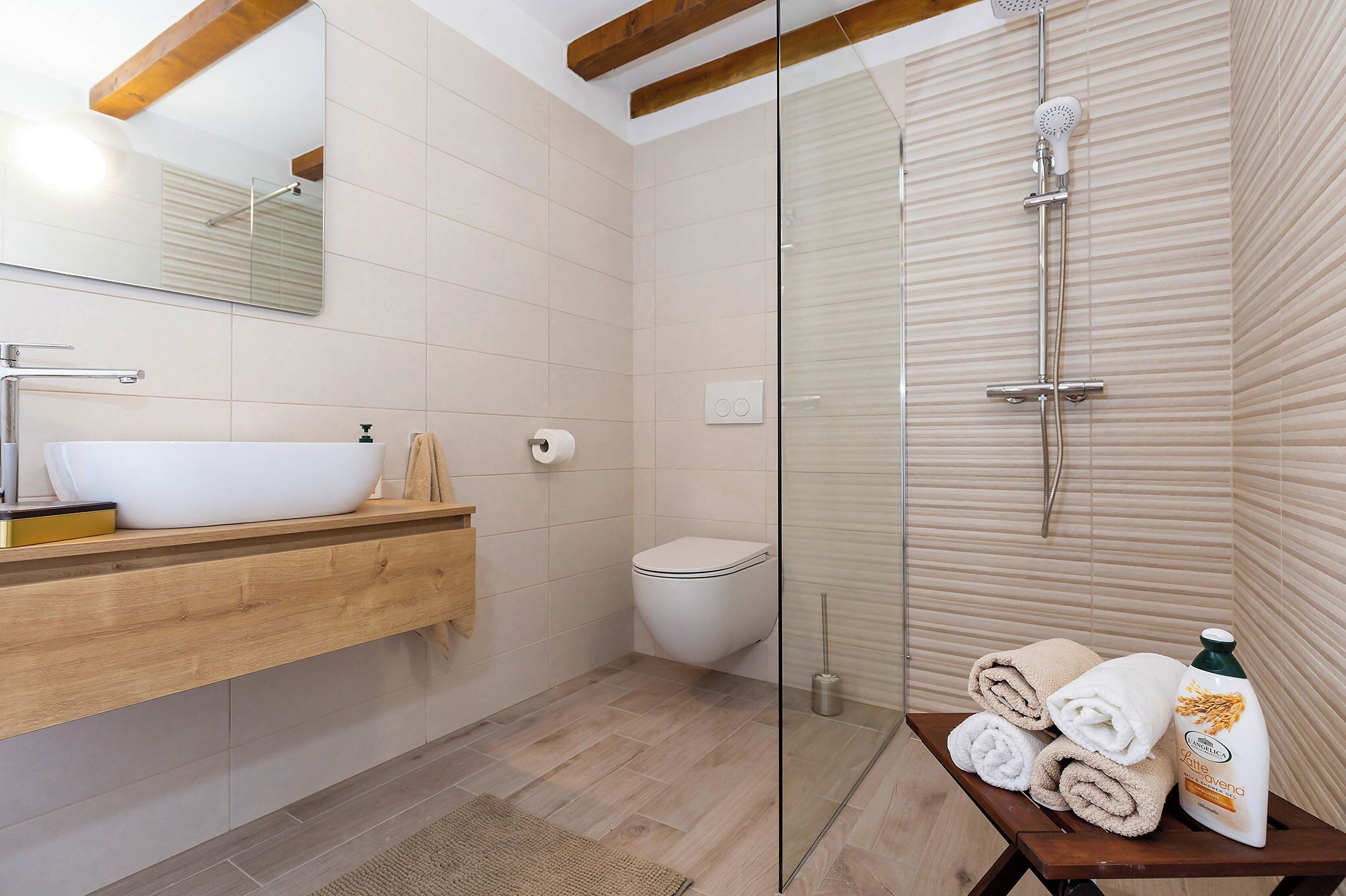 Un bagno moderno con doccia vetrata, mobile bagno in legno con lavandino bianco e servizi igienici.