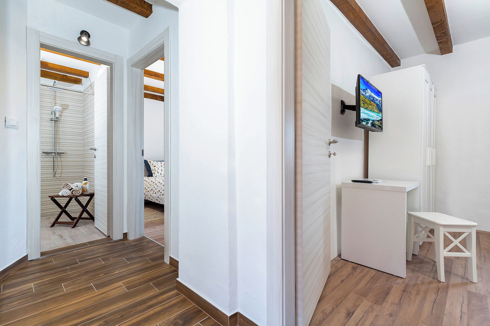 A modern bathroom with a shower, a small table with towels, and a TV mounted on a cabinet.