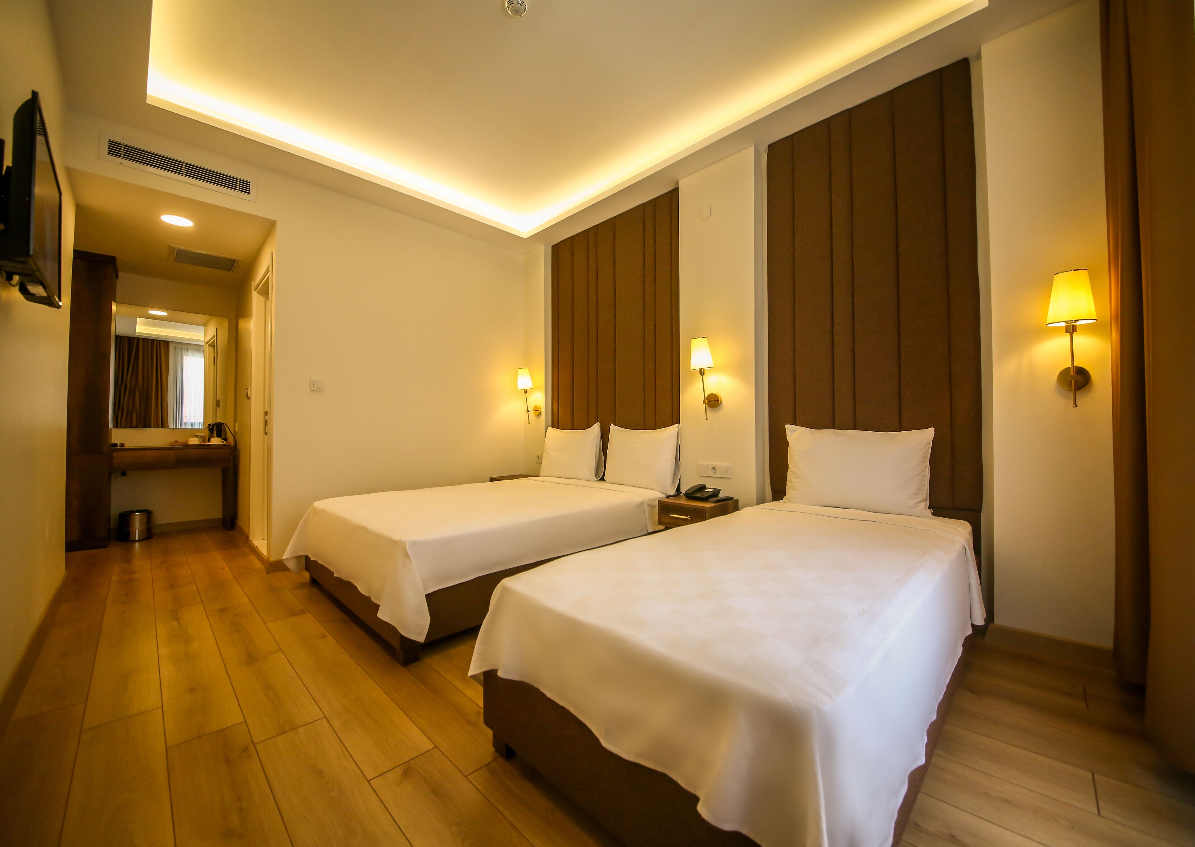 A hotel room with two beds, a small bedside table with a lamp, a mirror, and a wooden floor.