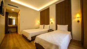 A hotel room with two beds, a small bedside table with a lamp, a mirror, and a wooden floor.