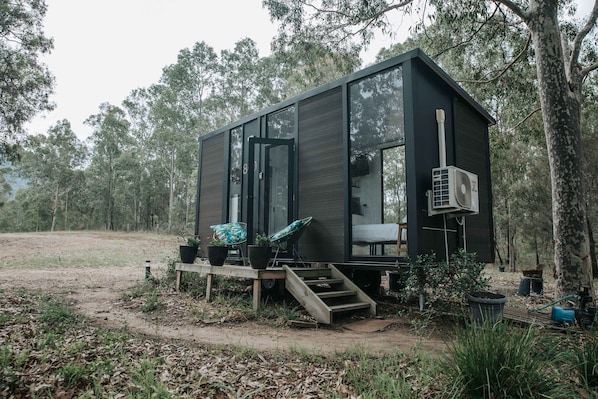 A modern cabin with a large window, a staircase, and a small porch area with outdoor seating.