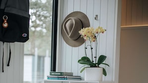 Une salle de bain avec un meuble-lavabo blanc, un chapeau accroché au mur et une orchidée en pot.