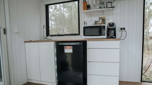 Une cuisine compacte avec des meubles blancs, un lave-vaisselle noir, un four à micro-ondes et une machine à café.